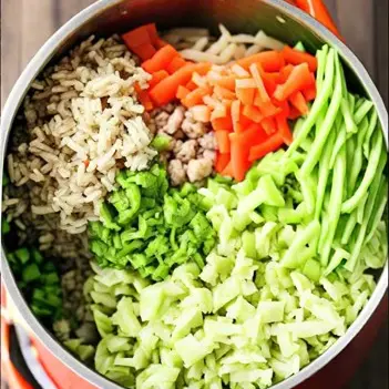 A pot brimming with fresh and vibrant ingredients including shredded carrots, zucchini, peas, baby spinach, and brown rice, ready to be transformed into a nutritious and flavorful homemade dog food recipe.